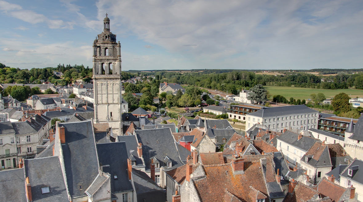 Panoramic view of an old French city with sloped rooftops and a bell tower in the distance